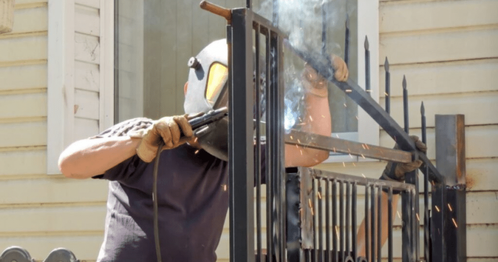 Worker welding a metal fence outside a house.